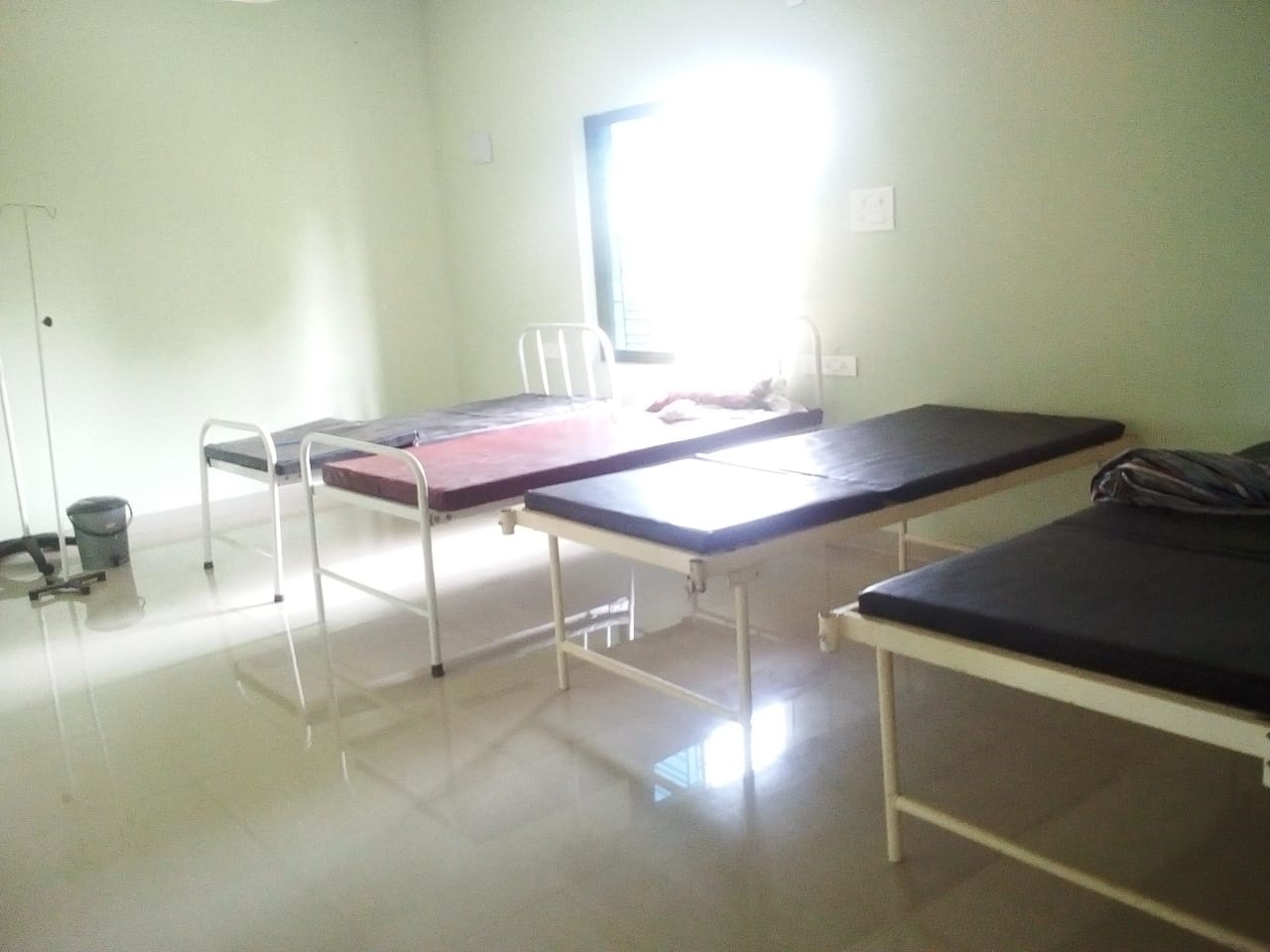 Room with four metal-frame beds with black mattresses and an IV stand