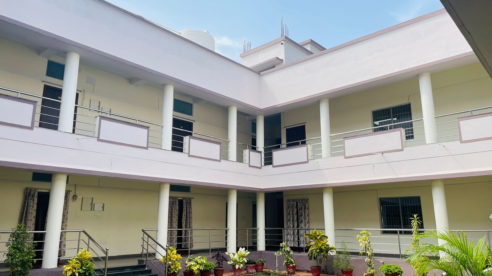 Two-storey pale building around a courtyard with potted plants and columns